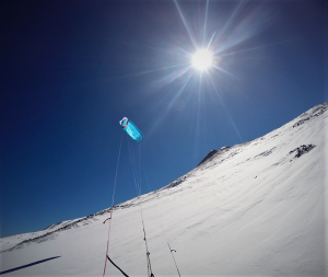 Das Bild zeigt einen blauen Kite ExploreV1 auf einem Berg mit weißem Schnee. Im Hintergrund ist der Himmel blau.