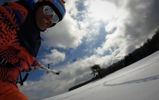 der Kiter wird durch peak5 von Flysurfer über den Schnee gezogen. Der Kiter fährt auf Ski. Der Snowkite wird vom Wind angetrieben.