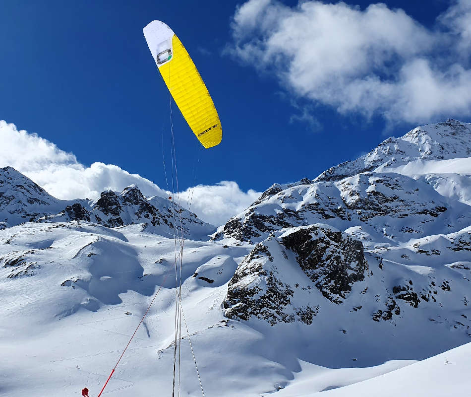 Der gelbe Kite EXPV1 von Ozonekites fliegt in den Bergen. Er zieht der Snowkiter von Snowkite-Odenwald mit den Ski am Passo bernina den Berg hoch.